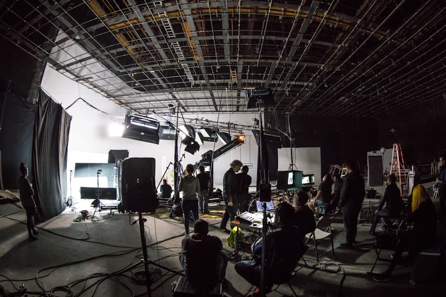 A large soundstage with overhead lighting rigs and a crew at work.